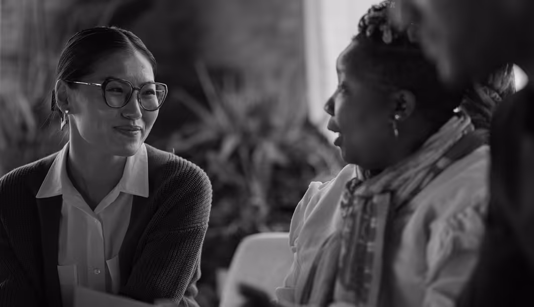 Two women engaged in conversation, one smiling and wearing glasses, black and white photo.